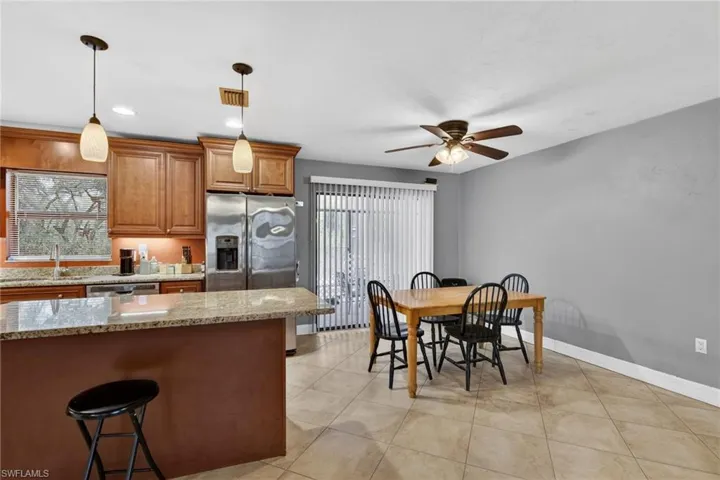Kitchen featuring light stone countertops, a breakfast bar, stainless steel appliances, wood finish cabinetry, and a ceiling fan