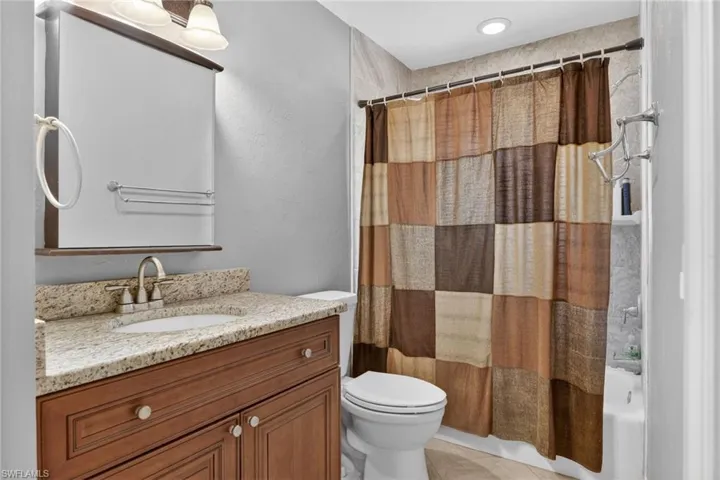 Full bath featuring vanity, shower / bath combo, light tile patterned floors, and a textured wall