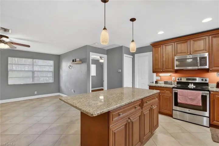 Kitchen featuring stainless steel appliances, wood finish cabinets, light stone countertops, pendant lighting, and light tile patterned flooring