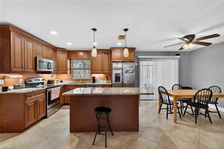 Kitchen with stainless steel appliances, a kitchen breakfast bar, wood finish cabinetry, hanging light fixtures, and a ceiling fan