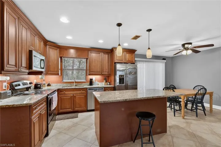 Kitchen featuring stainless steel appliances, light stone countertops, a kitchen island, wood finish cabinetry, and a breakfast bar