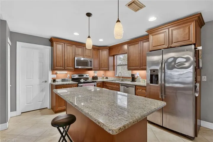 Kitchen featuring light stone counters, stainless steel appliances, wood finish cabinetry, hanging light fixtures, and a breakfast bar
