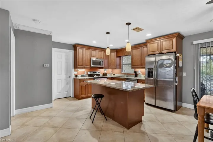 Kitchen featuring wood finish cabinets, a kitchen breakfast bar, stainless steel appliances, a center island, and light stone countertops