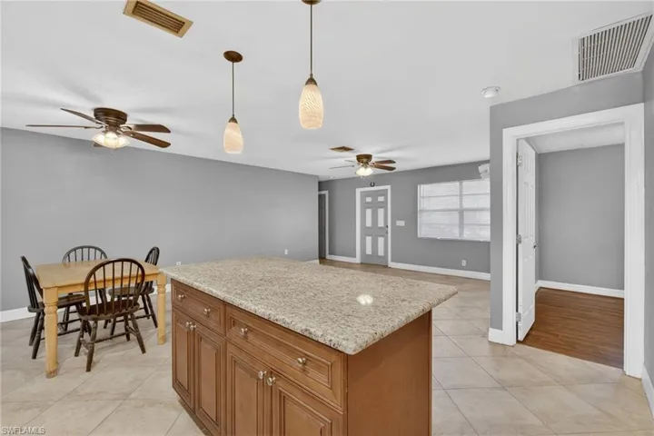 Kitchen featuring a center island, wood finish cabinetry, light stone counters, decorative light fixtures, and a ceiling fan