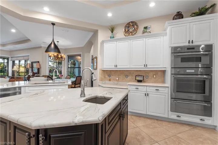 Kitchen featuring double oven, sink, a center island with sink, white cabinets, and hanging light fixtures