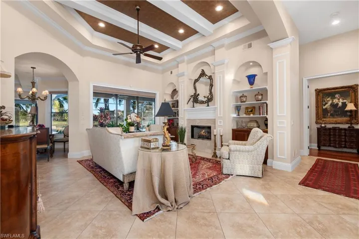 Living room with beamed ceiling, ceiling fan, built in features, and a high ceiling