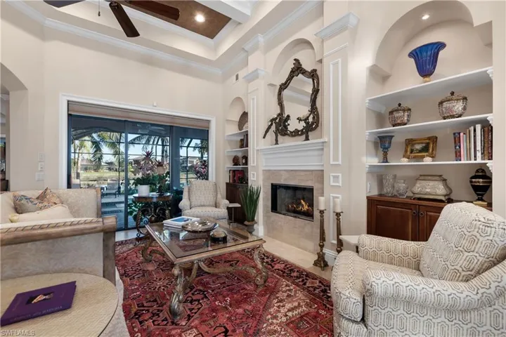 Living room featuring a tiled fireplace, crown molding, built in features, and a high ceiling