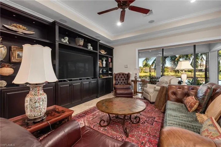 Tiled Family room featuring plenty of natural light, ceiling fan, ornamental molding, and a tray ceiling and a built-in wall of cabinetry.