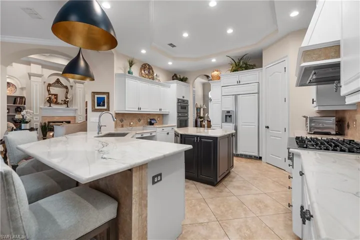 Kitchen featuring a raised ceiling, an island, 2 sinks, decorative backsplash, and stainless steel appliances