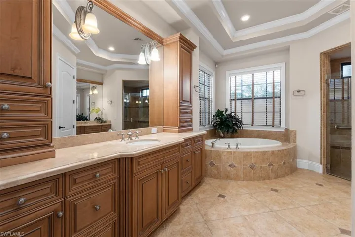 Bathroom featuring tile patterned flooring, plus walk in shower, a tray ceiling, and ornamental molding