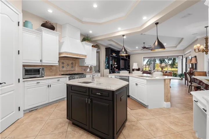 Kitchen featuring premium range hood, a tray ceiling, sink, and an island with sink