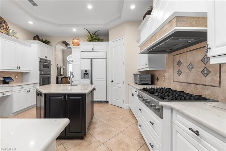 HUGE KITCHEN featuring white cabinetry, stainless steel appliances, premium range hood, an island with sink, and decorative backsplash