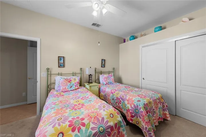 Carpeted bedroom with a ceiling fan, visible vents, and a closet