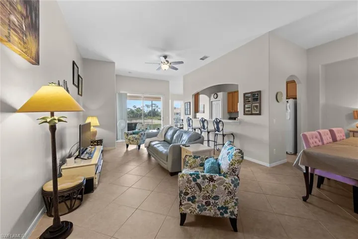 Living area with light tile patterned flooring, ceiling fan, arched walkways, baseboards, and visible vents