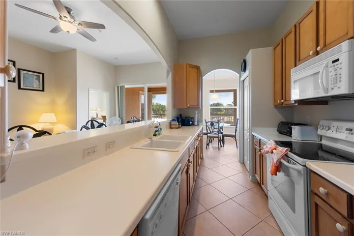 Kitchen with brown cabinets, light countertops, a sink, arched walkways, and white appliances