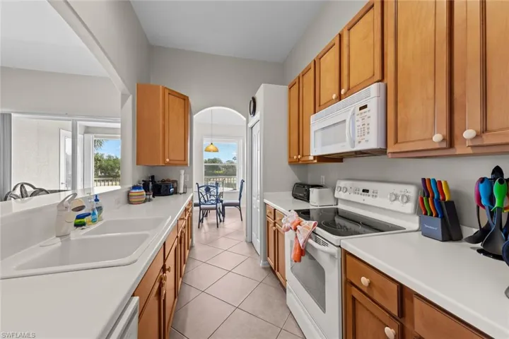 Kitchen with a sink, brown cabinets, white appliances, light tile patterned floors, and light countertops