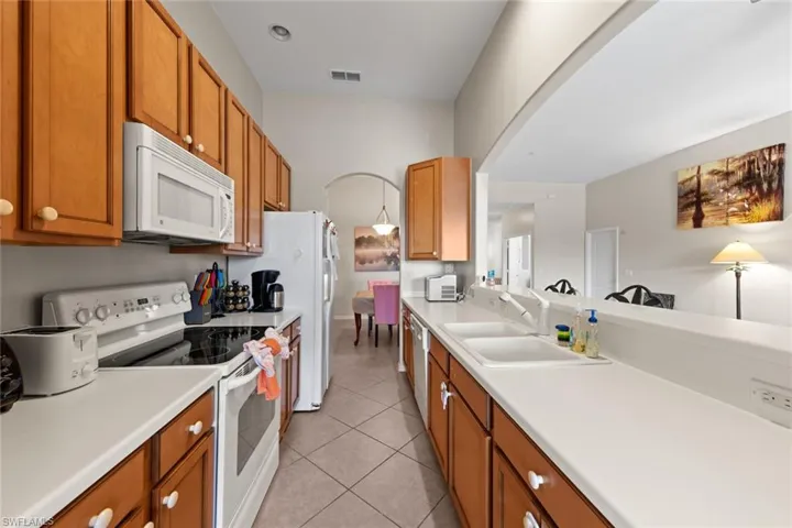 Kitchen featuring arched walkways, a sink, visible vents, white appliances, and light tile patterned floors