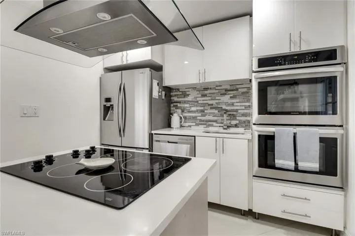 Kitchen with appliances with stainless steel finishes, extractor fan, white cabinetry, light countertops, and decorative backsplash