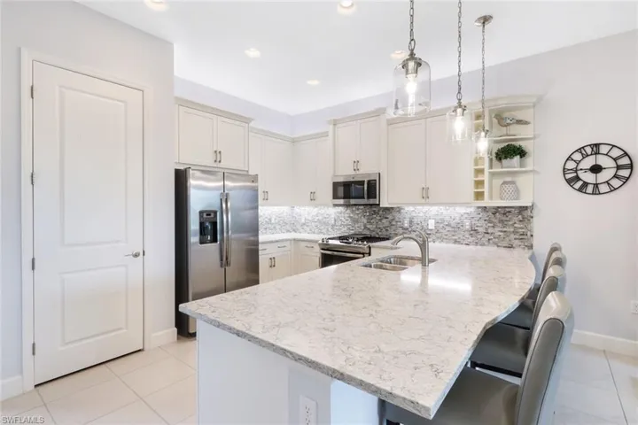 Kitchen with a breakfast bar, kitchen peninsula, stainless steel appliances, decorative light fixtures, and sink