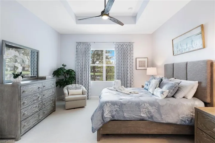 Carpeted bedroom featuring ceiling fan and a tray ceiling