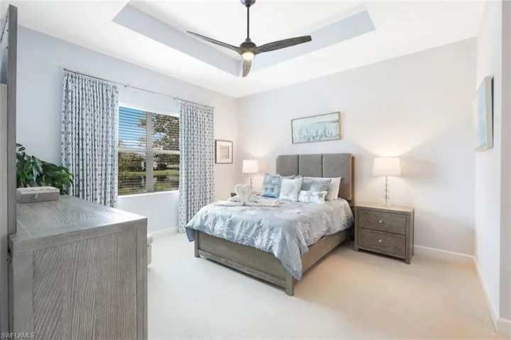 Carpeted bedroom with a tray ceiling and ceiling fan