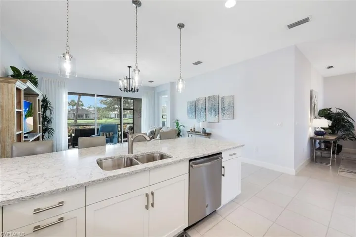 Kitchen with light stone counters, white cabinets, pendant lighting, sink, and stainless steel dishwasher