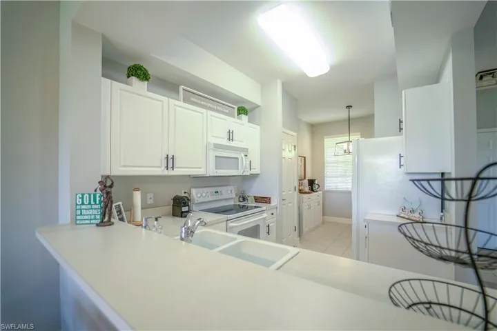 Kitchen with white appliances, light countertops, white cabinetry, and pendant lighting