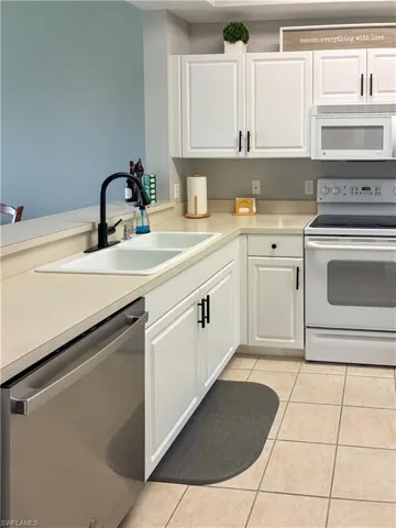 Kitchen featuring white appliances, white cabinetry, light countertops, and light tile patterned flooring
