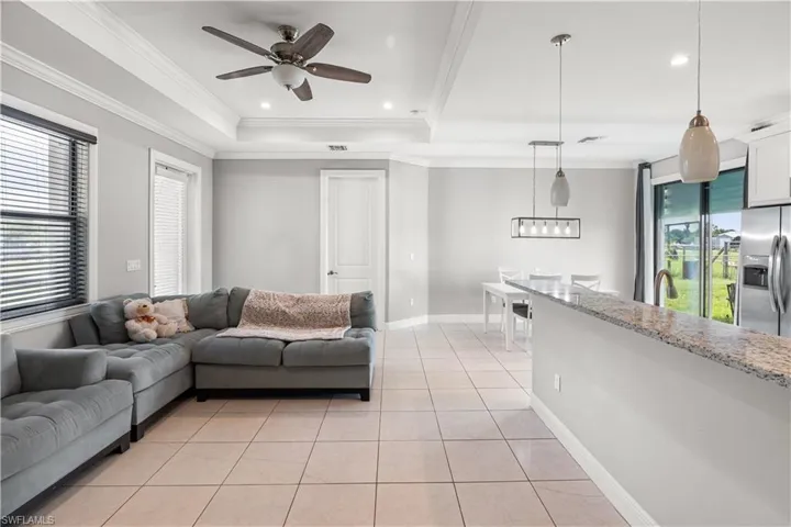 Living room with a tray ceiling, ceiling fan, light tile patterned floors, and ornamental molding
