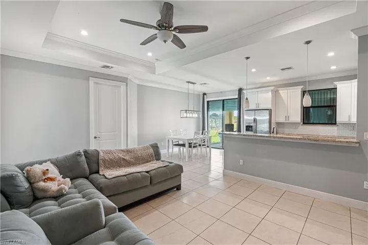 Living room featuring a raised ceiling, ceiling fan, ornamental molding, and light tile patterned floors