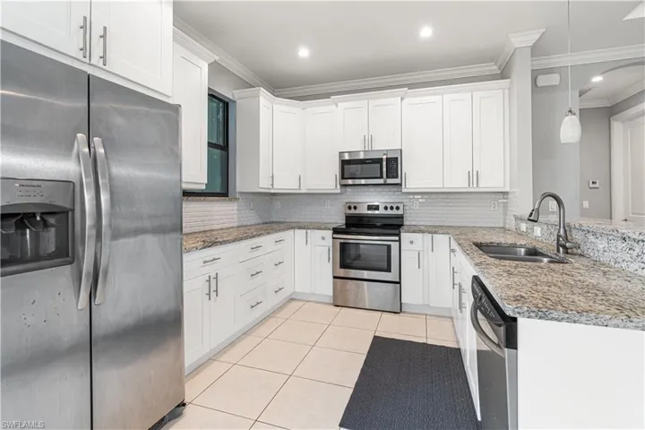 Kitchen featuring decorative light fixtures, stainless steel appliances, white cabinetry, and sink