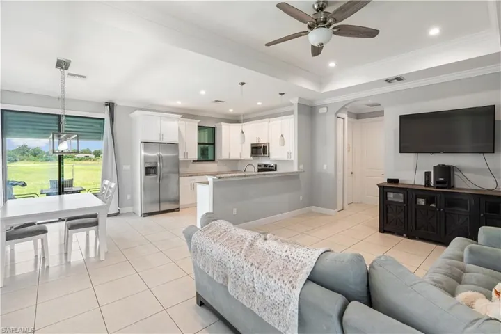 Living room featuring crown molding, a raised ceiling, light tile patterned flooring, and ceiling fan