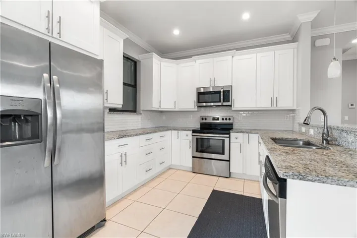 Kitchen featuring white cabinets, stainless steel appliances, sink, pendant lighting, and ornamental molding