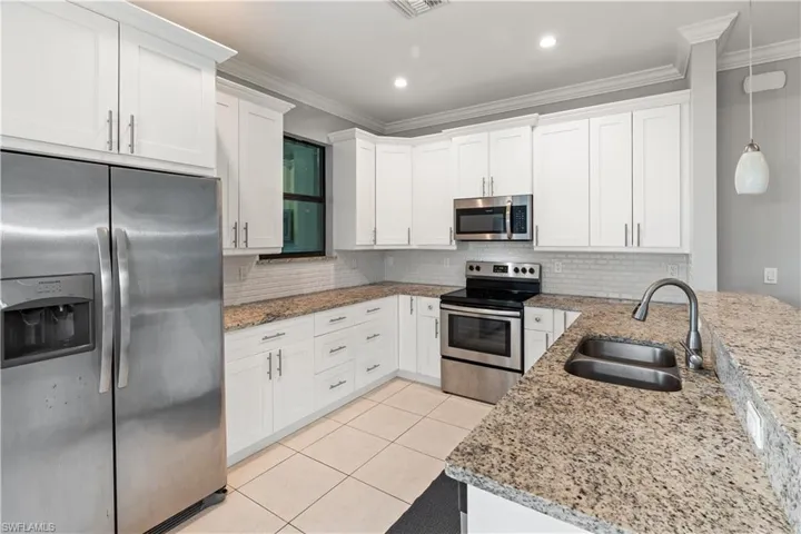 Kitchen with white cabinets, light stone countertops, stainless steel appliances, sink, and pendant lighting
