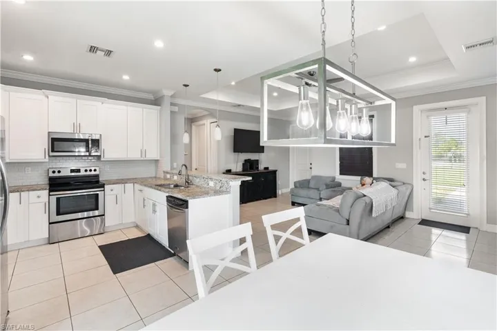 Kitchen featuring stainless steel appliances, decorative light fixtures, kitchen peninsula, sink, and a raised ceiling