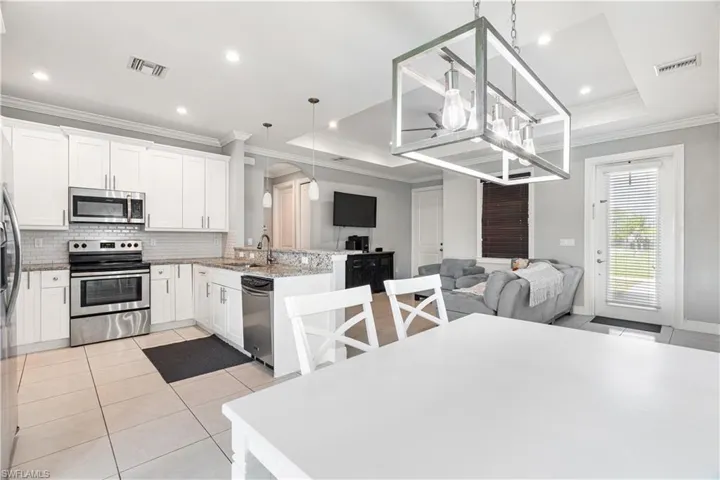 Kitchen with decorative light fixtures, appliances with stainless steel finishes, a tray ceiling, kitchen peninsula, and white cabinets