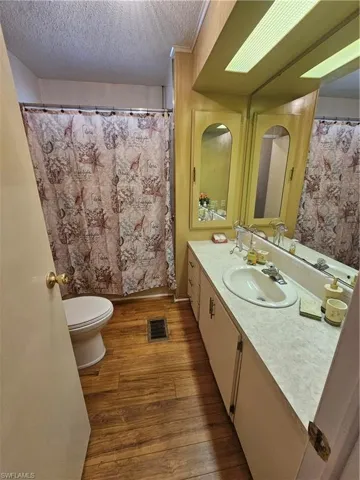 Full bath featuring visible vents, toilet, vanity, wood finished floors, and a textured ceiling