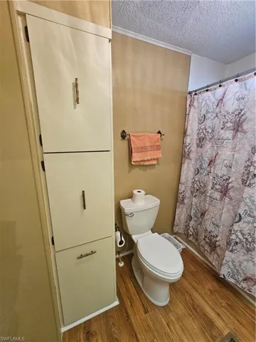Full bathroom with a shower with shower curtain, toilet, wood finished floors, and a textured ceiling