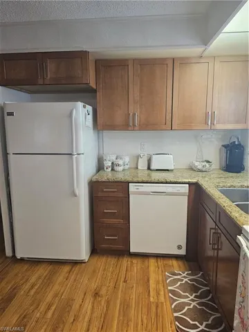 Kitchen with fridge, light stone countertops, dishwasher, and light wood-style flooring