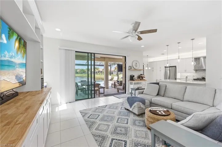 Open-concept living area featuring light tile flooring, built-in shelving with wood-finish countertop, and a ceiling fan