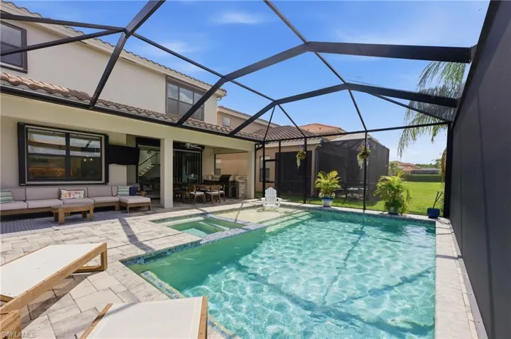 Screened-in outdoor living space featuring a paver patio, a rectangular swimming pool with an integrated spa, a covered lanai, and an exterior building facade