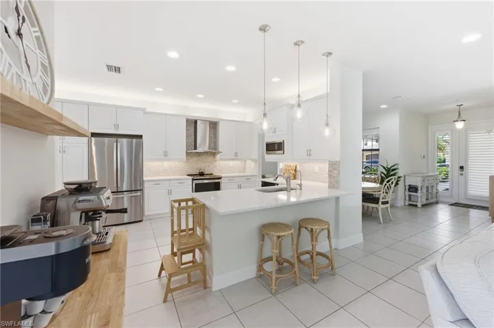 Modern kitchen featuring white shaker cabinetry, stainless steel appliances, a white stone countertop island with pendant lighting, and light tile flooring