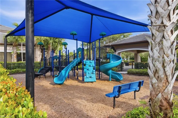 Playground area featuring a shade structure, multiple slides, climbing elements, and a ground covering of wood chips