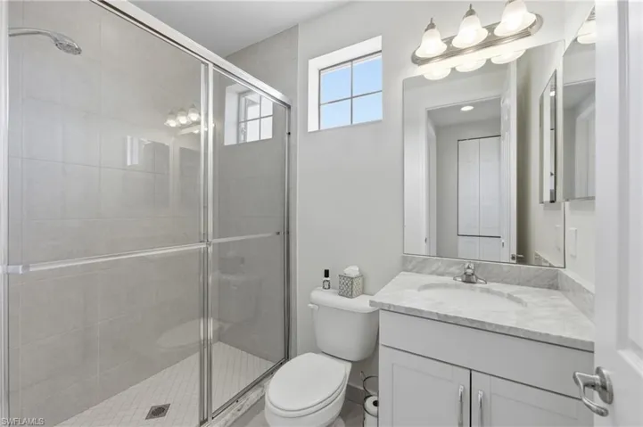 Bathroom featuring a glass-enclosed shower with tiled walls and floor, a single vanity with a stone countertop and integrated sink, a large mirror, and an overhead light fixture