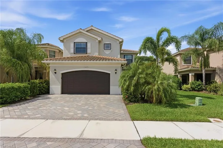 Two-story stucco residence featuring a tile roof, an arched garage door, and a paver driveway