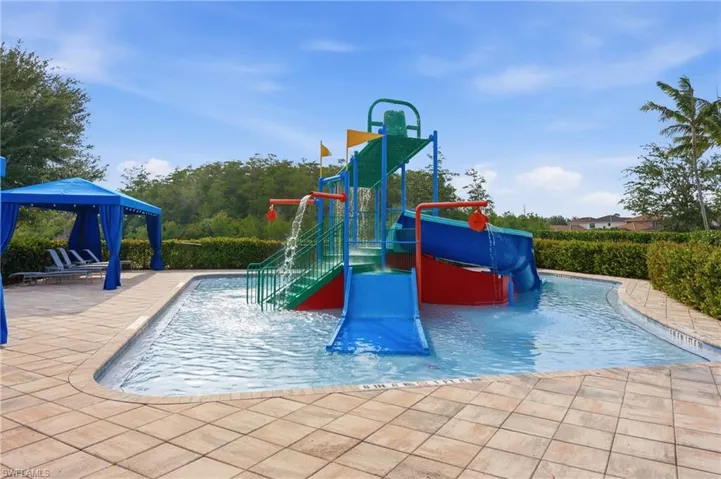 Outdoor amenity pool featuring a water play structure with multiple slides and water features, a free-form pool, and a poolside cabana with lounge seating