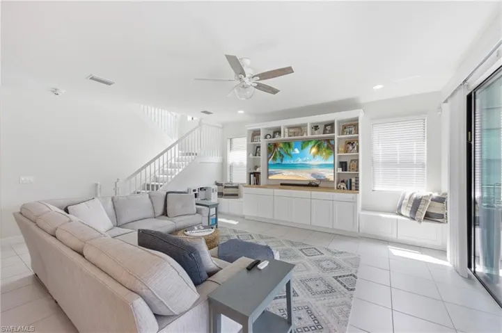 Living area featuring white tile flooring, a built-in entertainment center with shelving, a built-in window seat, a staircase with white railings, and sliding glass doors