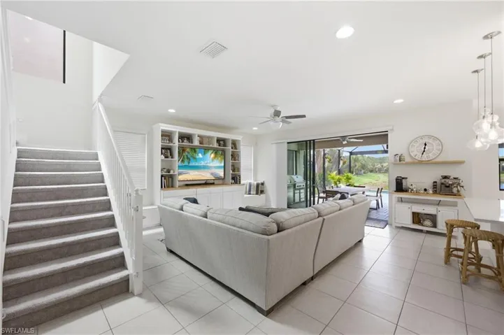 Spacious living area featuring tile flooring, a built-in media center with shelving, and large sliding glass doors opening to a screened outdoor space