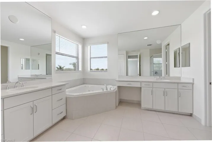 Spacious bathroom featuring a built-in corner soaking tub, dual vanity with white cabinetry and light-toned countertops, and expansive wall-mounted mirrors