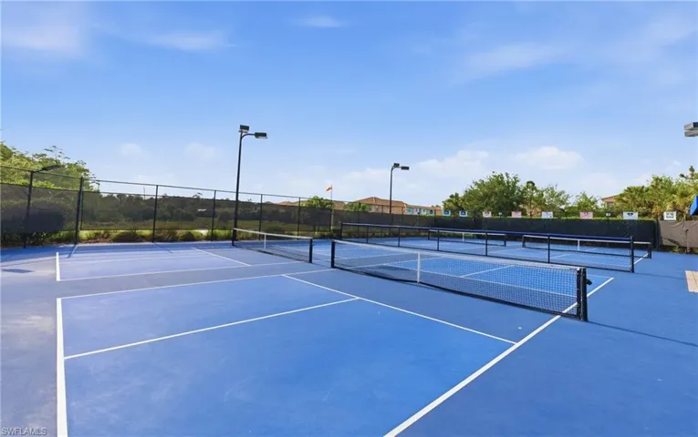 Multiple blue pickleball courts with white line markings, black netting, and surrounding black fencing